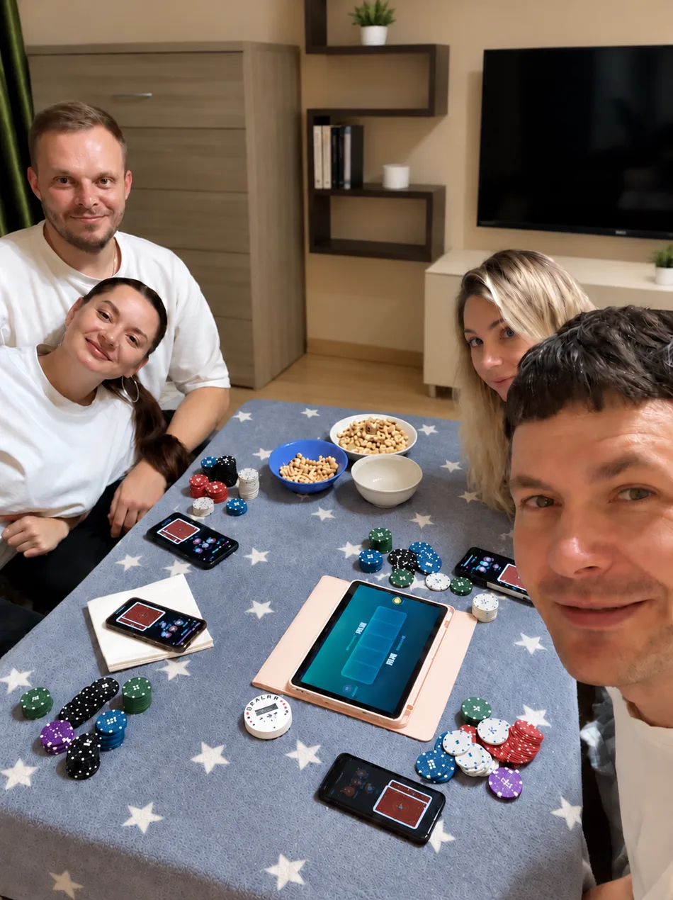 Four friends at a home poker table with chips, phones dealing cards and a tablet showing the board